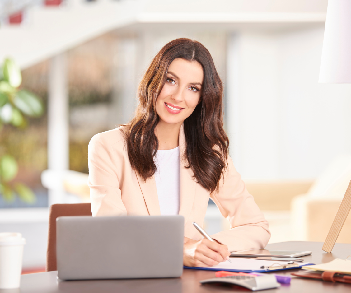 smiling woman sitting at a table with a laptop and a notebook
